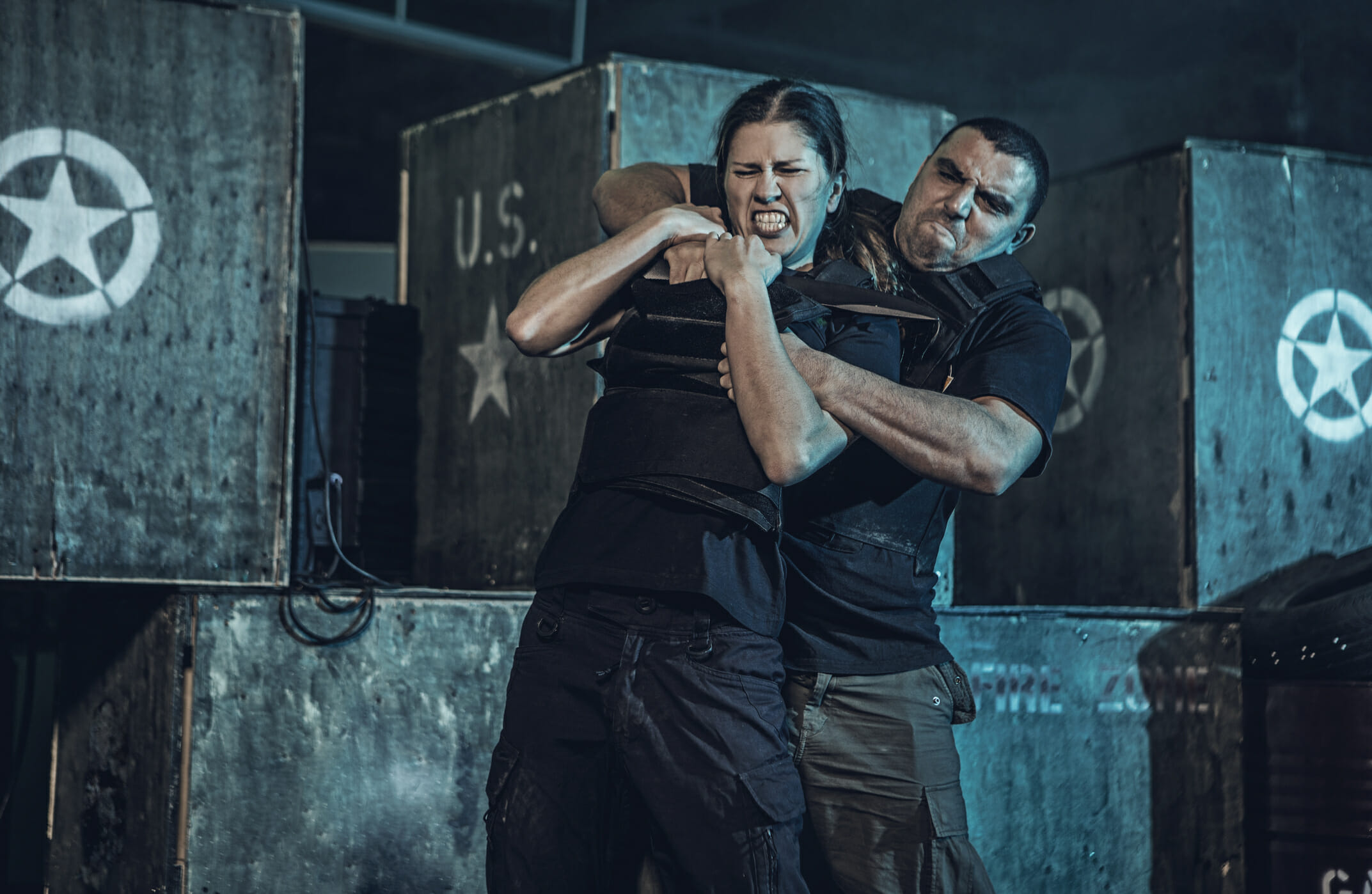 Young woman using Krav Maga fighting self defense against male assailant in dark indoor urban setting